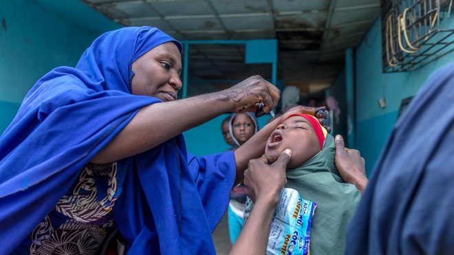 Un vaccinateur fournit à une jeune fille un vaccin oral contre la polio dans l'État de Kano, au Nigeria, en 2020