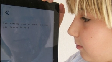 Un enfant devant un écran, sur lequel s'affiche un texte mis en page afin de favoriser l'exercice de la lecture. (image d'illustration)