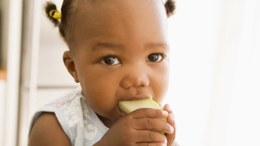 Une petite fille qui tente de manger une pomme