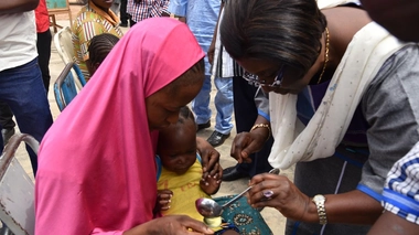 Le Représentant de l’OMS au Burkina Faso, Dr Alimata J. DIARRA-NAMA aidant une mère à administrer une dose de médicament de chimio prévention du paludisme à son enfant