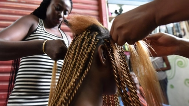 Une femme se fait tresser les cheveux dans un salon de coiffure au marché de Treicheville 